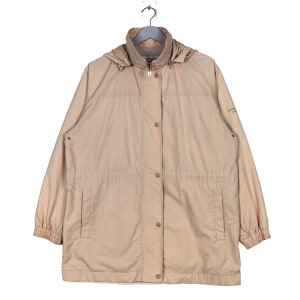 May include: A beige hooded jacket with a zipper and button closure. The jacket has a drawstring waist and two pockets. The jacket has the text "Columbia Sportswear Company" on the right sleeve.
