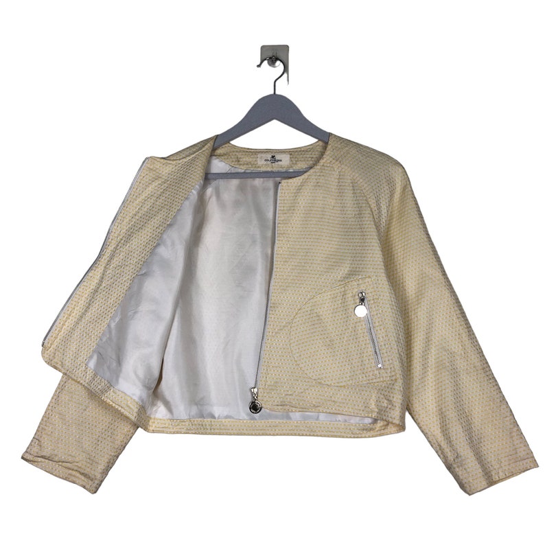 K&ouml;nnte beinhalten: Eine gelbe Jacke mit wei&szlig;em Muster und Rei&szlig;verschluss. Die Jacke hat eine kleine Tasche auf der rechten Seite mit einem silbernen Rei&szlig;verschluss.