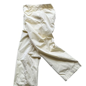 May include: Cream-colored, lightweight pants with a relaxed fit. The pants have a drawstring waistband and a straight leg design. The fabric appears to be slightly crinkled, giving it a casual look. The pants are made of a light, neutral-toned material.