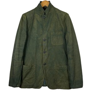 May include: A green jacket with a mandarin collar, three buttons, and two front pockets. The jacket is made of a textured fabric and hangs on a wooden hanger.