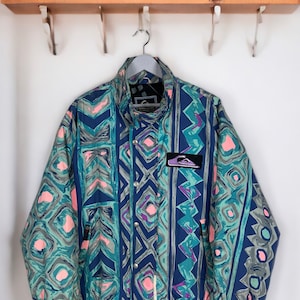 May include: A blue, green, pink, and purple patterned jacket with a zipper closure and a logo patch on the left sleeve. The jacket has a stand-up collar and a drawstring waist.