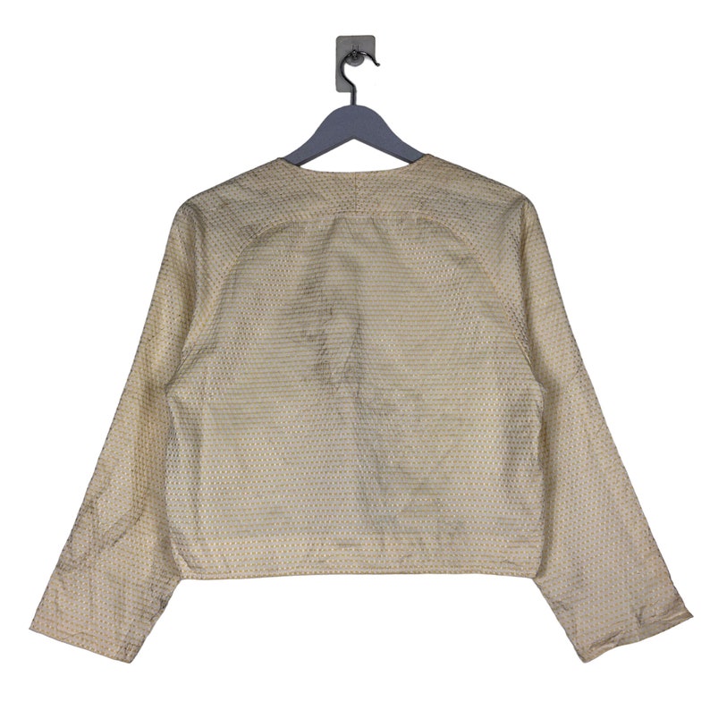 K&ouml;nnte beinhalten: Eine cremefarbene Jacke mit einem dezenten wei&szlig;en und cremefarbenen Muster. Die Jacke hat lange &Auml;rmel und einen Knopfverschluss vorne.