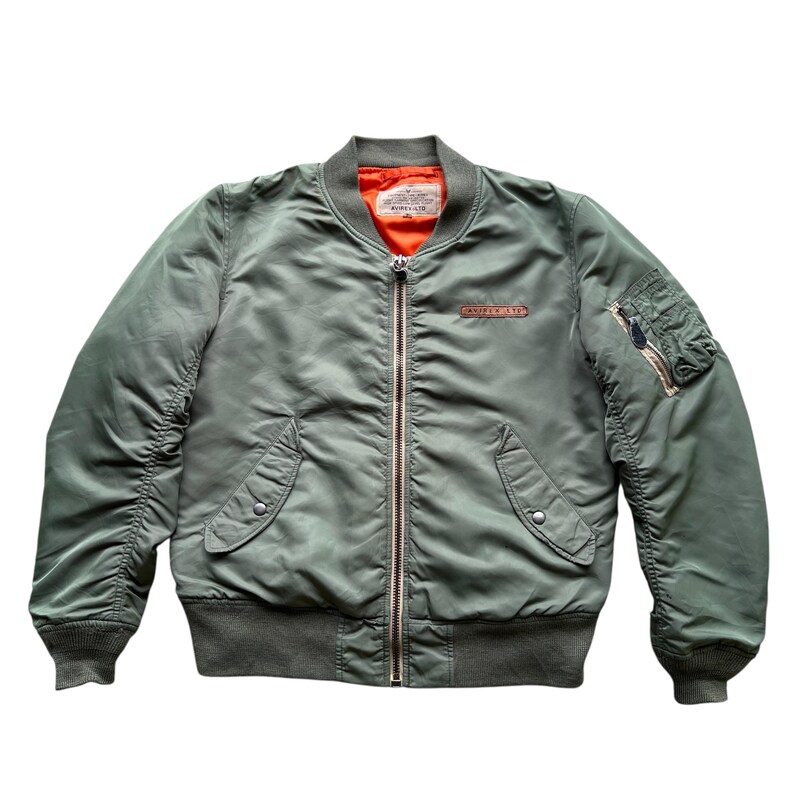 May include: An olive green bomber jacket featuring a bright orange interior lining, a full-length silver metal front zip, ribbed cuffs and hem, two front snap-button pockets, and a zipped utility pocket on the left sleeve with a leather pull.