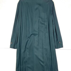 Może przedstawiać: Długi, ciemnozielony płaszcz z zapięciem na guziki i długimi rękawami. Płaszcz ma klasyczny kr&oacute;j z kołnierzem i dopasowanym krojem. Tkanina wydaje się być materiałem o średniej gramaturze, odpowiednim na chłodniejszą pogodę.