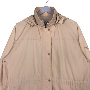 May include: A beige hooded jacket with a zipper closure and button accents. The jacket has a drawstring waist and a logo on the right sleeve that reads "Columbia Sportswear".