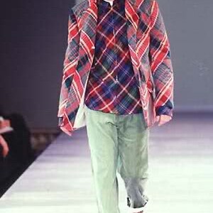 Puede incluir: Un hombre con una camisa a cuadros rojos y azules con una chaqueta a cuadros rojos y azules encima. Tambi&eacute;n lleva pantalones verdes y zapatos marrones.