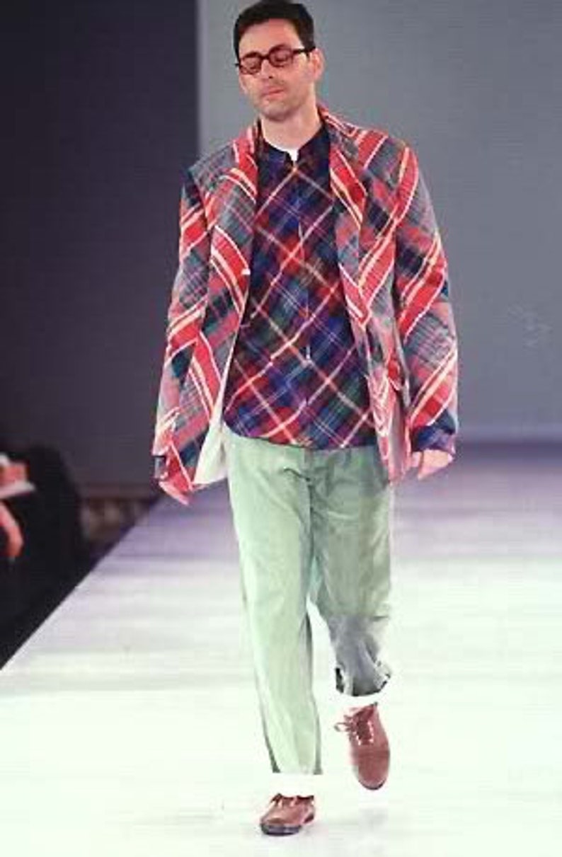 Puede incluir: Un hombre con una camisa a cuadros rojos y azules con una chaqueta a cuadros rojos y azules encima. Tambi&eacute;n lleva pantalones verdes y zapatos marrones.