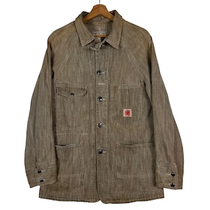 May include: Brown workwear jacket with a collared neckline, button-up front, and multiple pockets. The jacket features a small red and white patch on the front pocket and is hanging on a wooden hanger.
