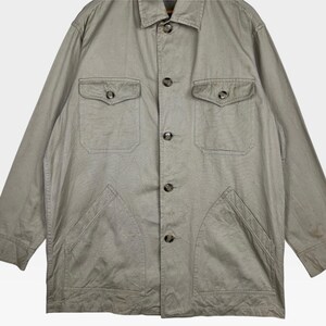 K&ouml;nnte beinhalten: Hellolivgr&uuml;ne Jacke mit Knopfleiste, zwei Brusttaschen und zwei unteren Taschen. Die Jacke hat einen Kragen und lange &Auml;rmel. Der Stoff scheint eine leichte Baumwoll- oder Leinenmischung zu sein.