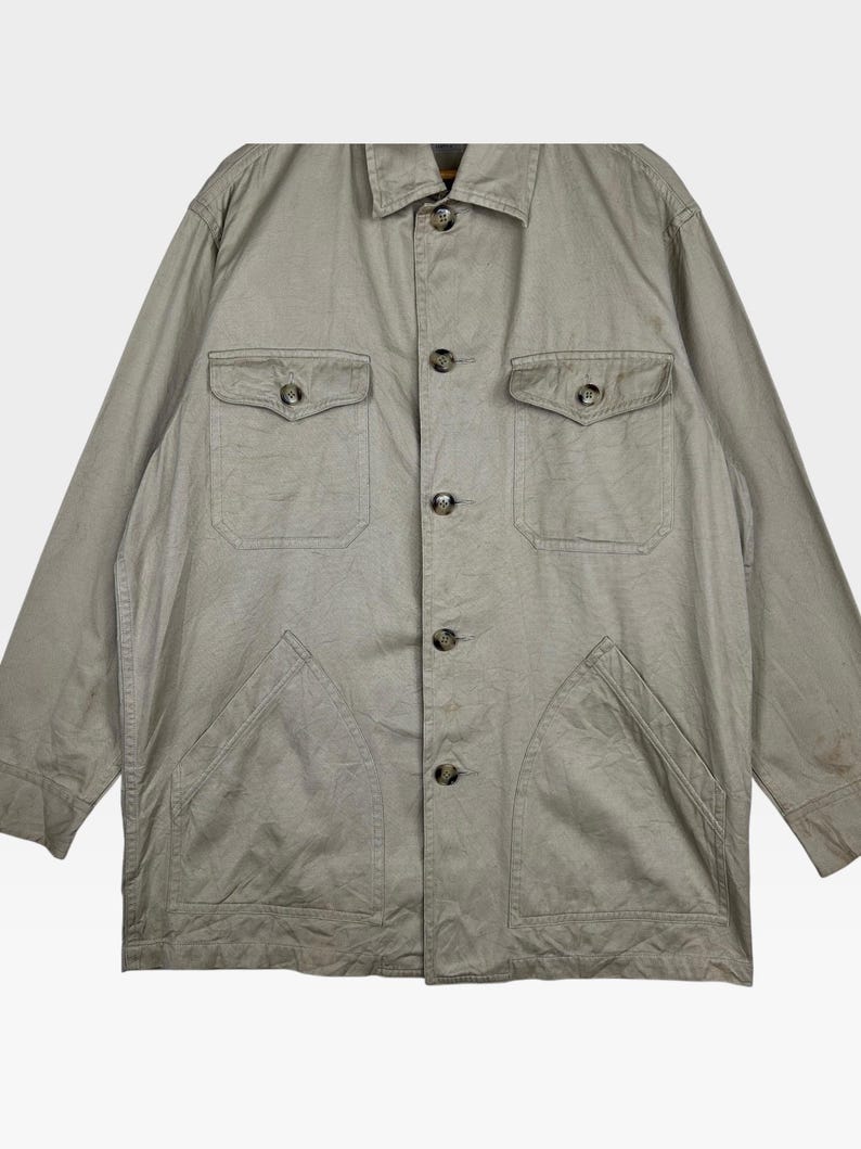 K&ouml;nnte beinhalten: Hellolivgr&uuml;ne Jacke mit Knopfleiste, zwei Brusttaschen und zwei unteren Taschen. Die Jacke hat einen Kragen und lange &Auml;rmel. Der Stoff scheint eine leichte Baumwoll- oder Leinenmischung zu sein.