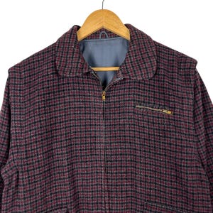 Puede incluir: Chaqueta a cuadros burdeos y negros con cierre de cremallera completo y un peque&ntilde;o bolsillo con cremallera en el pecho. La chaqueta tiene cuello y est&aacute; colgada de una percha de madera.