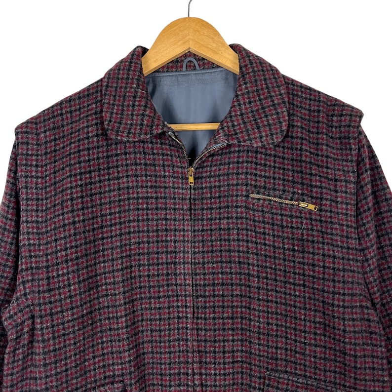 Puede incluir: Chaqueta a cuadros burdeos y negros con cierre de cremallera completo y un peque&ntilde;o bolsillo con cremallera en el pecho. La chaqueta tiene cuello y est&aacute; colgada de una percha de madera.