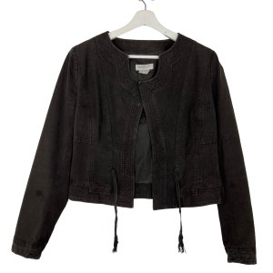 May include: A dark brown corduroy jacket with a distinctive collar and two front pockets. The jacket has long sleeves and a cropped length. It features decorative ties at the waist and is hung on a white hanger.