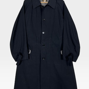 May include: A black trench coat with a collared neckline and button-down closure. The coat features long sleeves with adjustable straps at the cuffs and a knee-length hem. It is hanging on a wooden hanger.