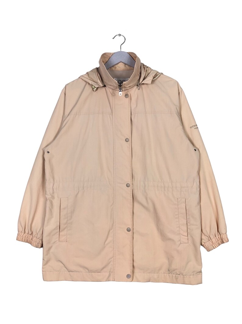 May include: A beige hooded jacket with a zipper and button closure. The jacket has two pockets and a drawstring waist.