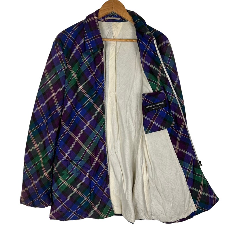 Puede incluir: Una chaqueta de cuadros azules, verdes y morados con cierre de cremallera. La chaqueta tiene un forro blanco y un peque&ntilde;o bolsillo en el interior. La etiqueta dice "COMME des GARCONS HOMME PLUS".