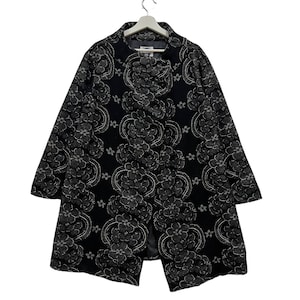 May include: A black coat featuring a floral design in grey and silver tones. The coat has a notched collar and long sleeves. The fabric has a textured finish. The coat is suspended from a white hanger.