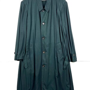 Może przedstawiać: Długi, ciemnozielony płaszcz z zapięciem na guziki, kołnierzem i kieszeniami. Płaszcz ma długie rękawy i klasyczny kr&oacute;j, odpowiedni na r&oacute;żne okazje. Płaszcz jest wykonany z gładkiej tkaniny.