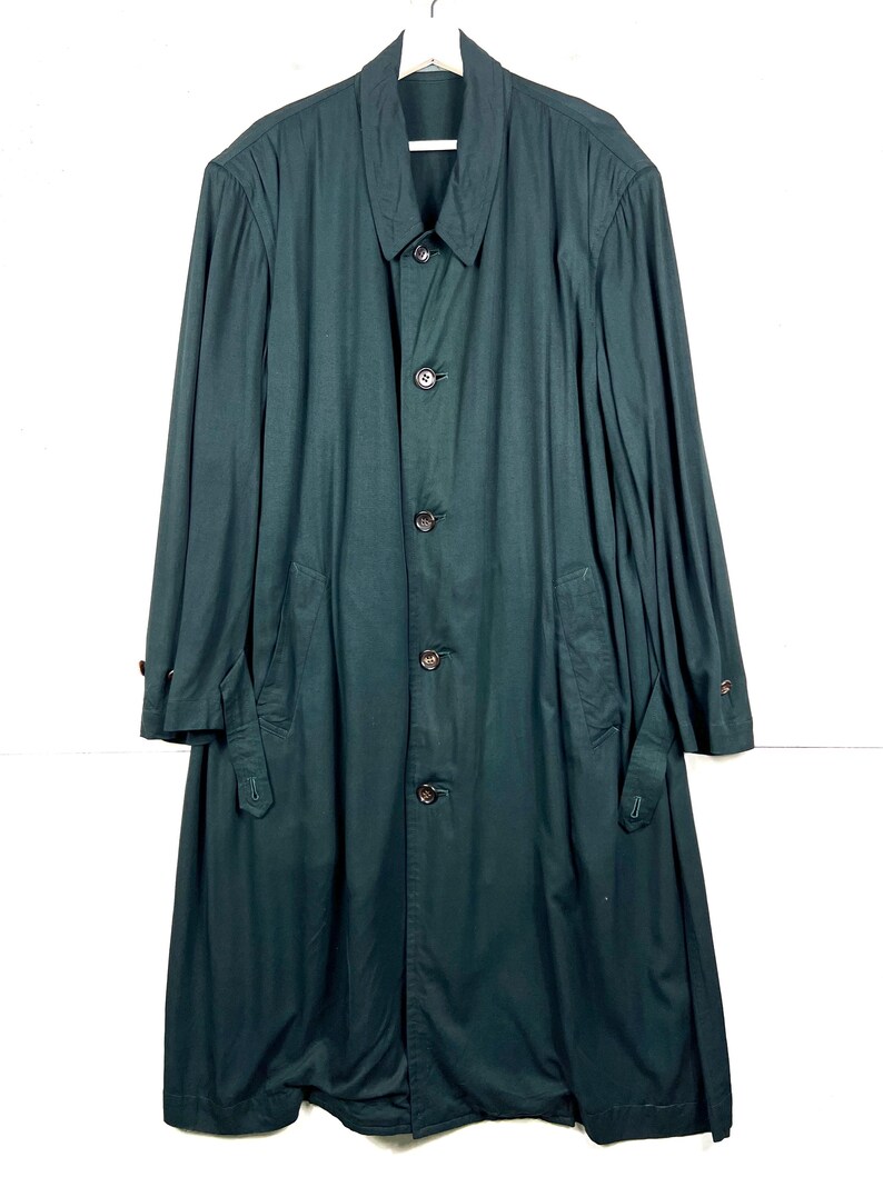 Może przedstawiać: Długi, ciemnozielony płaszcz z zapięciem na guziki, kołnierzem i kieszeniami. Płaszcz ma długie rękawy i klasyczny kr&oacute;j, odpowiedni na r&oacute;żne okazje. Płaszcz jest wykonany z gładkiej tkaniny.