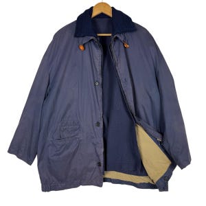 Könnte beinhalten: Eine blaue Jacke mit braunem Kragen und Reißverschluss. Die Jacke hat einen Knopfleisten vorne und eine Tasche auf der linken Seite.