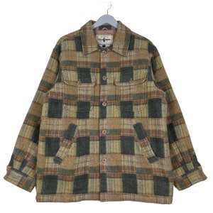 May include: A tan, green, and gray plaid jacket with a button-up front, two chest pockets, and two side pockets. The jacket is hanging on a gray hanger. The label on the jacket reads "DAZEE".