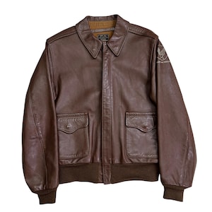 May include: A brown leather bomber jacket with a collared neckline, two front pockets, and ribbed cuffs and hem. The jacket features an Air Force emblem on the upper left sleeve. The jacket is a classic style.