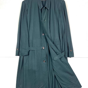 Może przedstawiać: Długi, ciemnozielony płaszcz z zapięciem na guziki i paskiem. Płaszcz wisi na białym wieszaku na białym tle. Płaszcz ma klasyczny kr&oacute;j z kołnierzem i długimi rękawami.