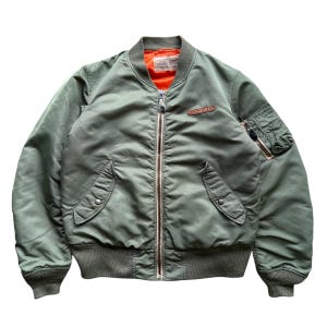 May include: An olive green bomber jacket featuring a bright orange interior lining, a full-length front zip, ribbed cuffs and hem, two snap-button side pockets, a zipped utility pocket on the left sleeve, and a leather patch on the chest.