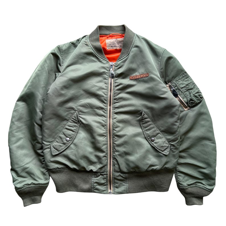 May include: An olive green bomber jacket featuring a bright orange interior lining, a full-length front zip, ribbed cuffs and hem, two snap-button side pockets, a zipped utility pocket on the left sleeve, and a leather patch on the chest.