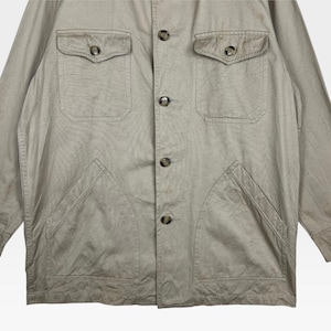K&ouml;nnte beinhalten: Beige Jacke mit vier Vordertaschen und Kn&ouml;pfen. Die Jacke hat zwei Brusttaschen mit Knopfverschluss und zwei untere aufgesetzte Taschen. Die Kn&ouml;pfe sind dunkelbraun.