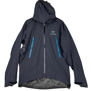May include: A dark navy blue hooded jacket with a full-length zip and two front pockets with bright blue zips. The jacket features the brand name "Arc'teryx" on the chest.