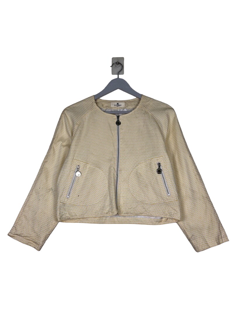 K&ouml;nnte beinhalten: Eine gelbe Jacke mit wei&szlig;em Muster, Rei&szlig;verschluss und zwei Taschen. Die Jacke hat einen runden Ausschnitt und lange &Auml;rmel.