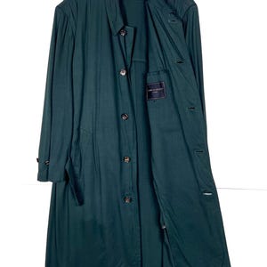 Może przedstawiać: Długi, ciemnozielony płaszcz z zapięciem na guziki i wykładanym kołnierzem. Płaszcz wisi na białym wieszaku na białym tle. Płaszcz ma kieszeń z metką w środku.