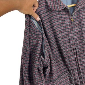Puede incluir: Primer plano de una chaqueta con estampado de pata de gallo en tonos burdeos, negro y gris. La chaqueta tiene cuello, cierre de cremallera y un bolsillo con cremallera gris. La chaqueta se abre para mostrar el interior.