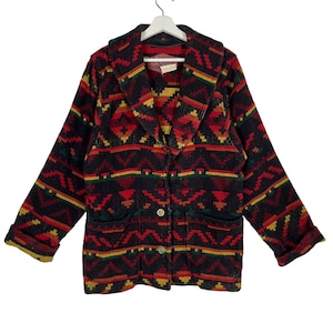 Puede incluir: Un blazer negro con un estampado geométrico en rojo, amarillo y verde. El blazer tiene solapas, dos bolsillos delanteros y dos botones dorados. Las mangas están dobladas.
