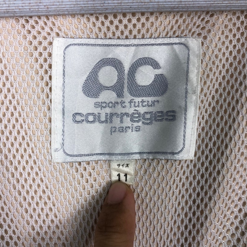 May include: White label with black text that reads "sport futur courr&egrave;ges paris" and a logo of the letters "ac" in a circle. The label is attached to a white mesh fabric with a white tag that reads "11" in black.