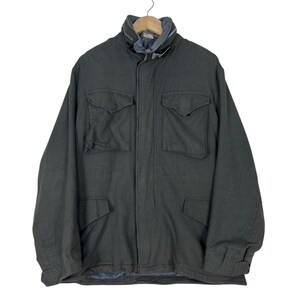 Puede incluir: Una chaqueta de campo gris carbón oscuro que presenta un cuello alto con un compartimento oculto para capucha, un cierre frontal de cremallera completa con tapeta de botones a presión y cuatro bolsillos grandes con solapas abotonadas.