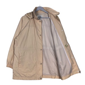 May include: A beige hooded jacket with a zipper and button closure. The jacket has a mesh lining and a drawstring hood.
