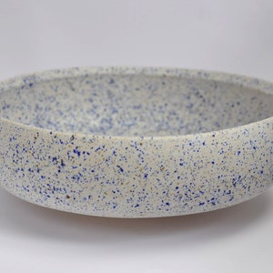May include: A white ceramic bowl with a speckled blue and white glaze. The bowl is round and has a wide rim.