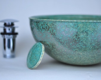 May include: A large, round, teal-coloured ceramic bowl with a speckled finish. The bowl is sitting on a white surface.