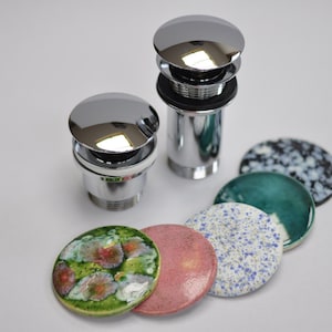 May include: Two chrome bathroom sink drain stoppers with five different colored ceramic drain covers. The covers are in shades of green, blue, white, pink, and green with white accents.