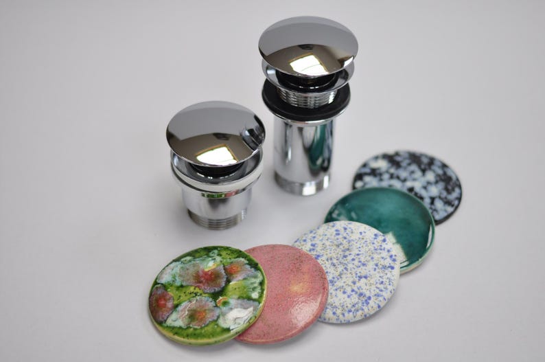 May include: Two chrome bathroom sink drain stoppers with five different colored ceramic drain covers. The covers are in shades of green, blue, white, pink, and green with white accents.