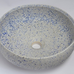 May include: White ceramic bowl with a blue speckled glaze. The bowl has a round shape and a small drainage hole in the center.