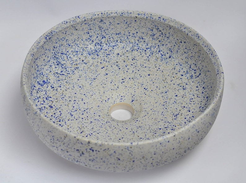 May include: White ceramic bowl with a blue speckled glaze. The bowl has a round shape and a small drainage hole in the center.