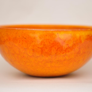 May include: A bright orange ceramic bowl with a textured surface. The bowl is round and has a smooth, glossy finish.