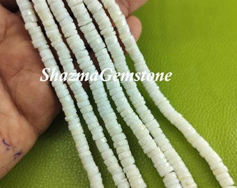 May include: A strand of white opal beads, each bead is faceted and has a slightly irregular shape. The beads are strung on a clear thread and are approximately 6mm in diameter. The beads are displayed on a hand against a green background.