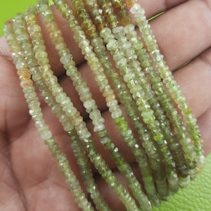 Pode incluir: Um fio de contas de pedras preciosas verdes e amarelas. As contas são facetadas e têm uma forma ligeiramente irregular. O fio tem aproximadamente 45 cm de comprimento.