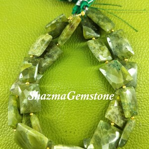 May include: A strand of green gemstone beads with a green tassel. The beads are faceted and have a slightly irregular shape. The beads are strung on a gold wire.