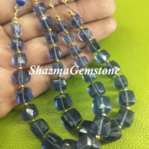 May include: Three strands of blue gemstone beads with gold spacers. The beads are faceted and have a square shape. The beads are strung on a thin cord.