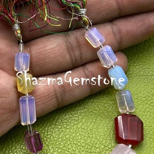 Könnte beinhalten: Eine farbenfrohe Edelsteinkette mit einer Vielzahl facettierter, rechteckiger Perlen in Gelb-, Lila-, Blau-, Rosa- und Rottönen. Die Halskette hat eine mehrfarbige Quaste oben und den Text "Shazma Gemstone".